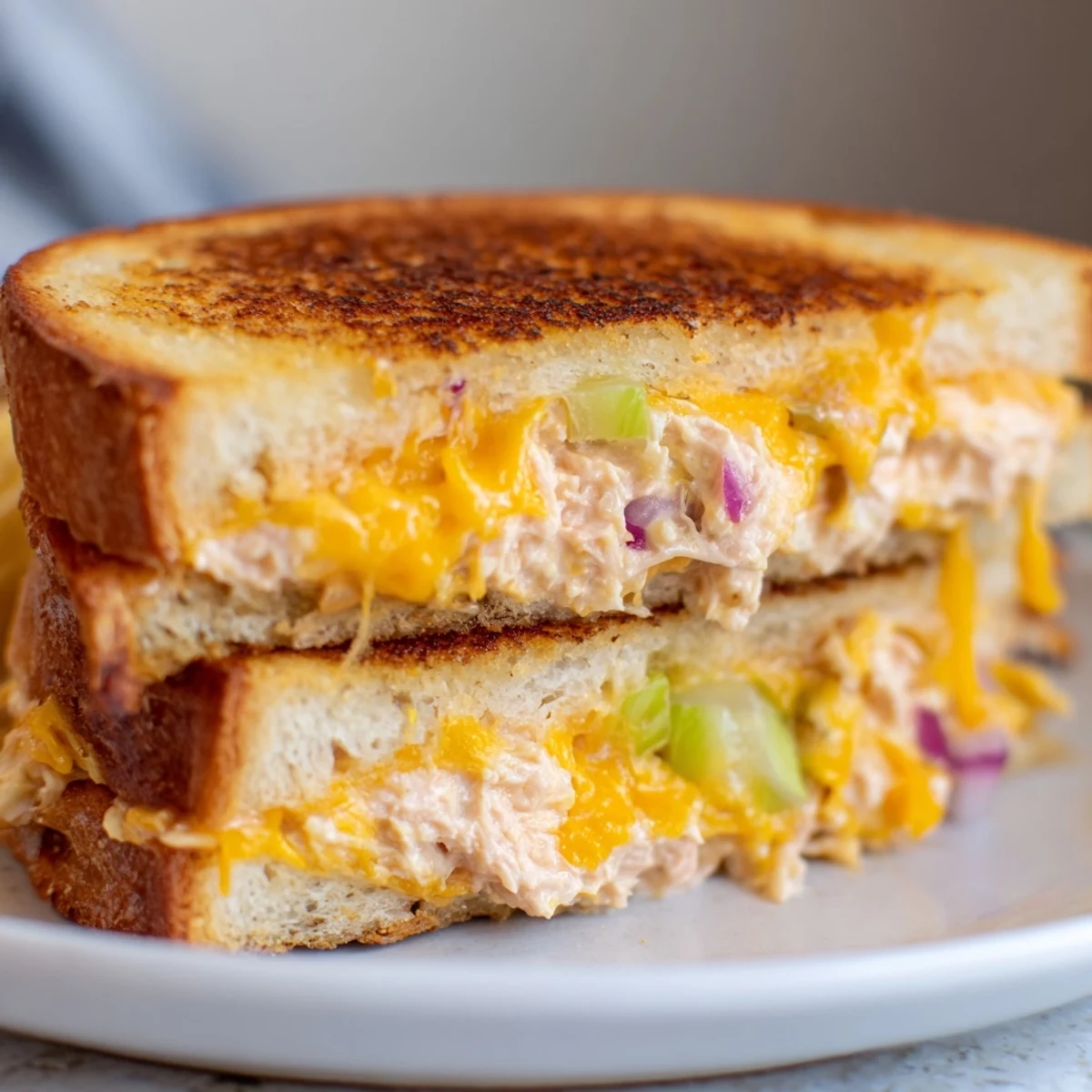 A fully assembled Spicy Tuna Melt sandwich with toasted sourdough bread, melted cheese, and fresh tomato slices on a wooden cutting board.