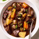 Close-up of hearty earthy beef stew with tender beef and vegetables next to fresh bread.
