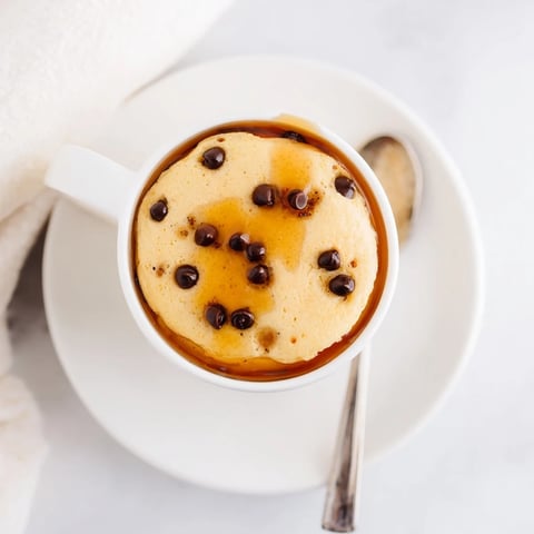 A fluffy, warm Microwave Mug Pancake topped with a pat of butter and drizzled with maple syrup, ready to eat straight from the mug.