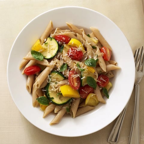 A close-up of Garden Veggie Pasta with zucchini, yellow squash, and blistered tomatoes on a rustic wooden table.