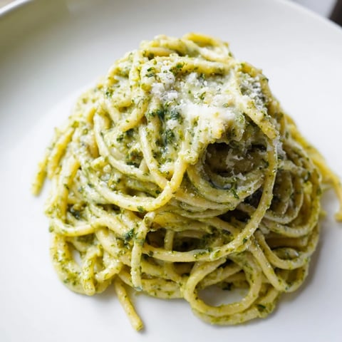 A close-up of Creamy Sunflower Seed Pesto Pasta twirled on a fork, glistening with vibrant green sauce and fresh basil leaves.
