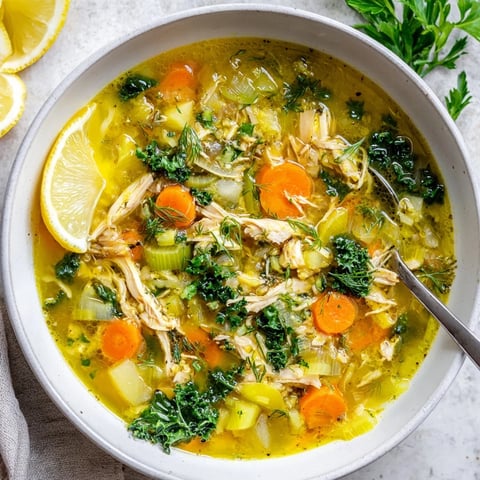 A bowl of High Protein Lemon and Turmeric Chicken Soup, featuring tender shredded chicken, vibrant baby kale, and a golden, aromatic broth.