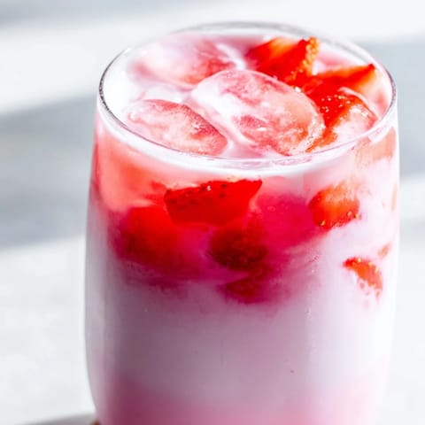 Two glasses of Refresher Copycat Pink Drink garnished with sliced strawberries, ready to enjoy on a warm afternoon.  