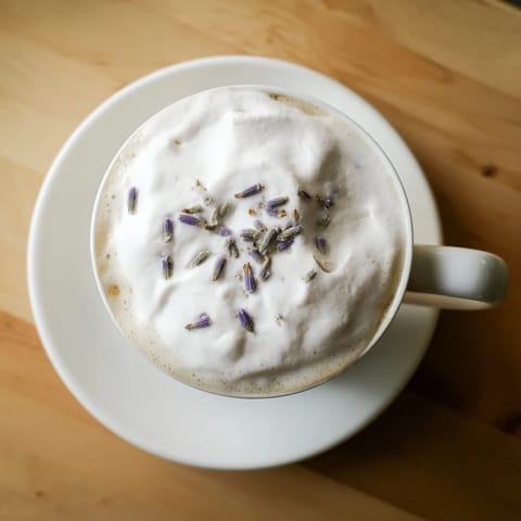 Two elegant glasses of Whipped Lavender Latte garnished with dried lavender beside shortbread cookies on a rustic table.