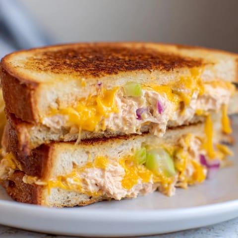 A fully assembled Spicy Tuna Melt sandwich with toasted sourdough bread, melted cheese, and fresh tomato slices on a wooden cutting board.