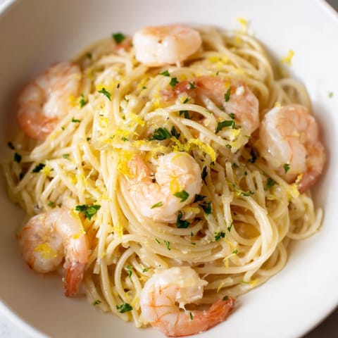 A close-up of Lemon Garlic Shrimp Pasta showing juicy shrimp over spaghetti, with a bright, silky lemon garlic butter sauce and a sprinkle of Parmesan.