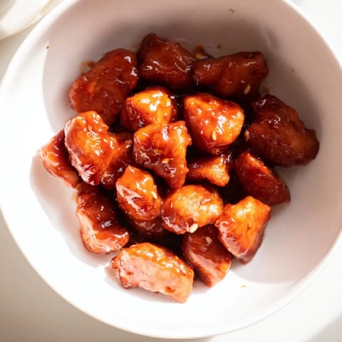 A close-up of the Sweet Chili Chicken Bowl reveals tender chicken pieces coated in a glossy, tangy-sweet glaze over fluffy rice.