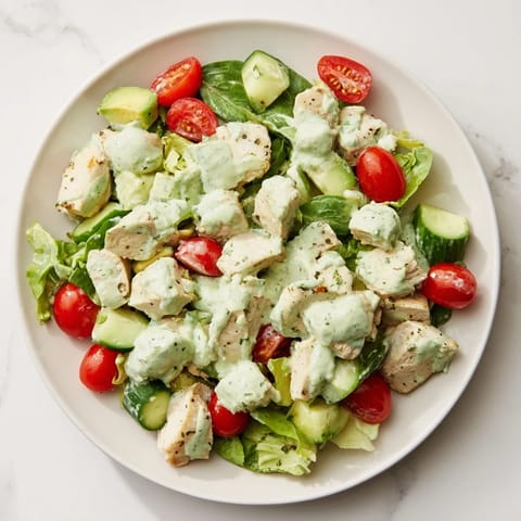 Warm chicken salad served with avocado ranch dressing, red onions, celery, and ripe cherry tomatoes on a bed of greens.  