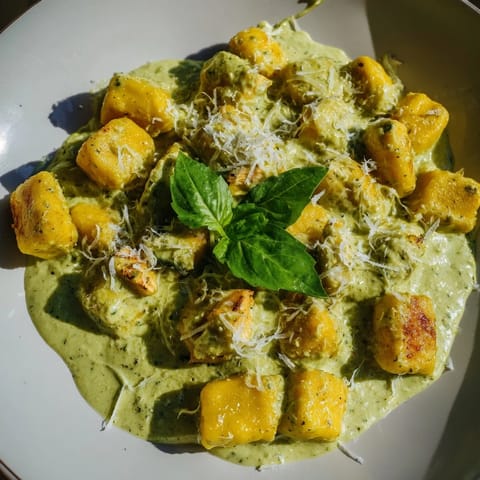 A close-up of tender gnocchi and juicy chicken in rich pesto cream, served hot as a comforting main.