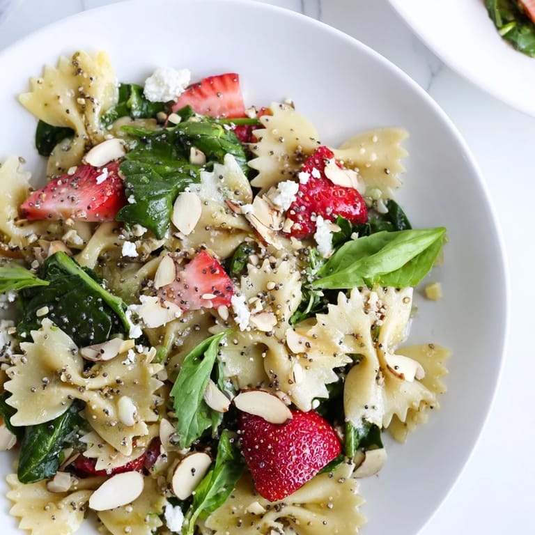 A close-up of the colorful Spring Spinach Strawberry Pasta Salad drizzled with poppy seed dressing and topped with creamy feta.
